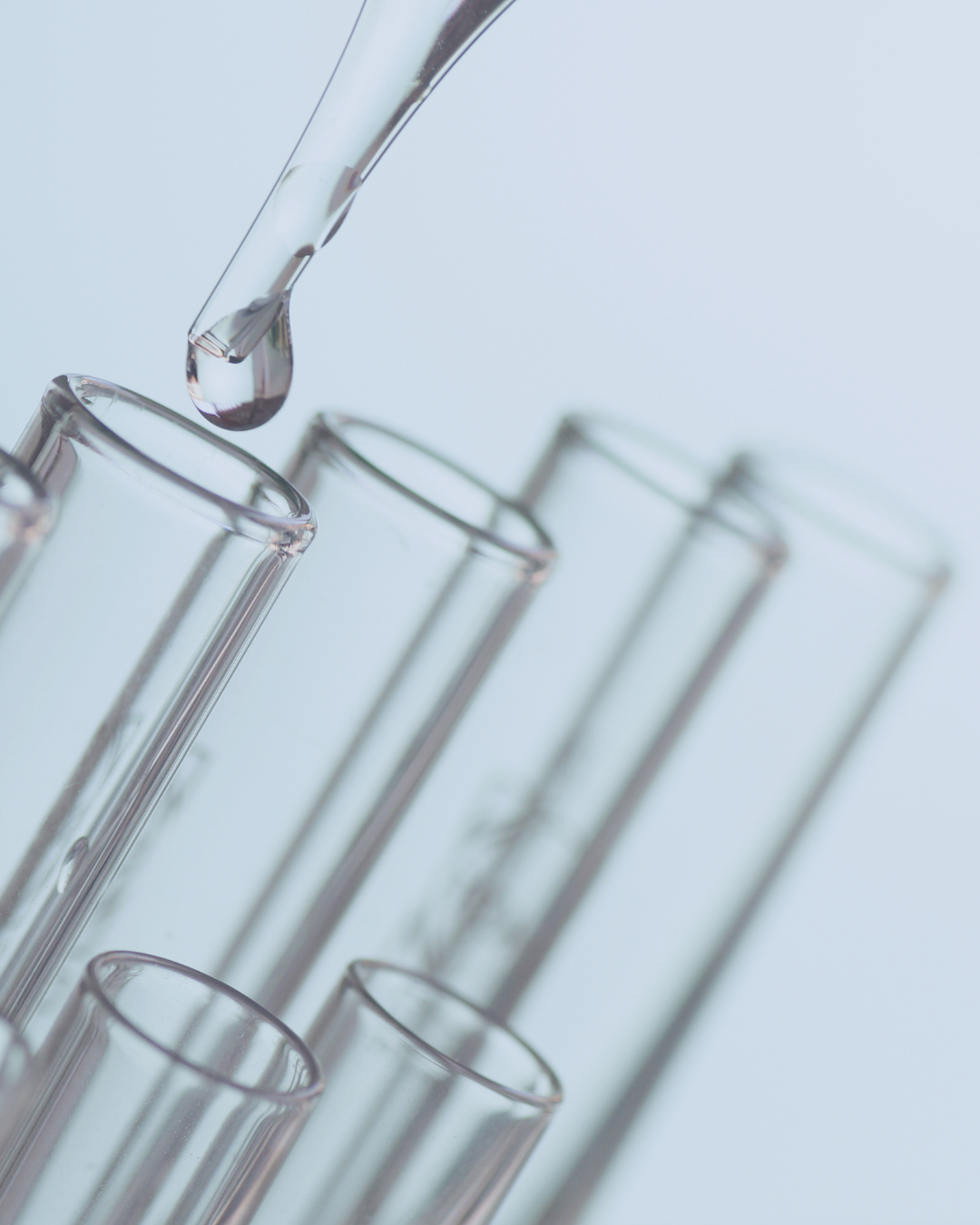 Glass dropper adding liquid to a test tube against a light gray background